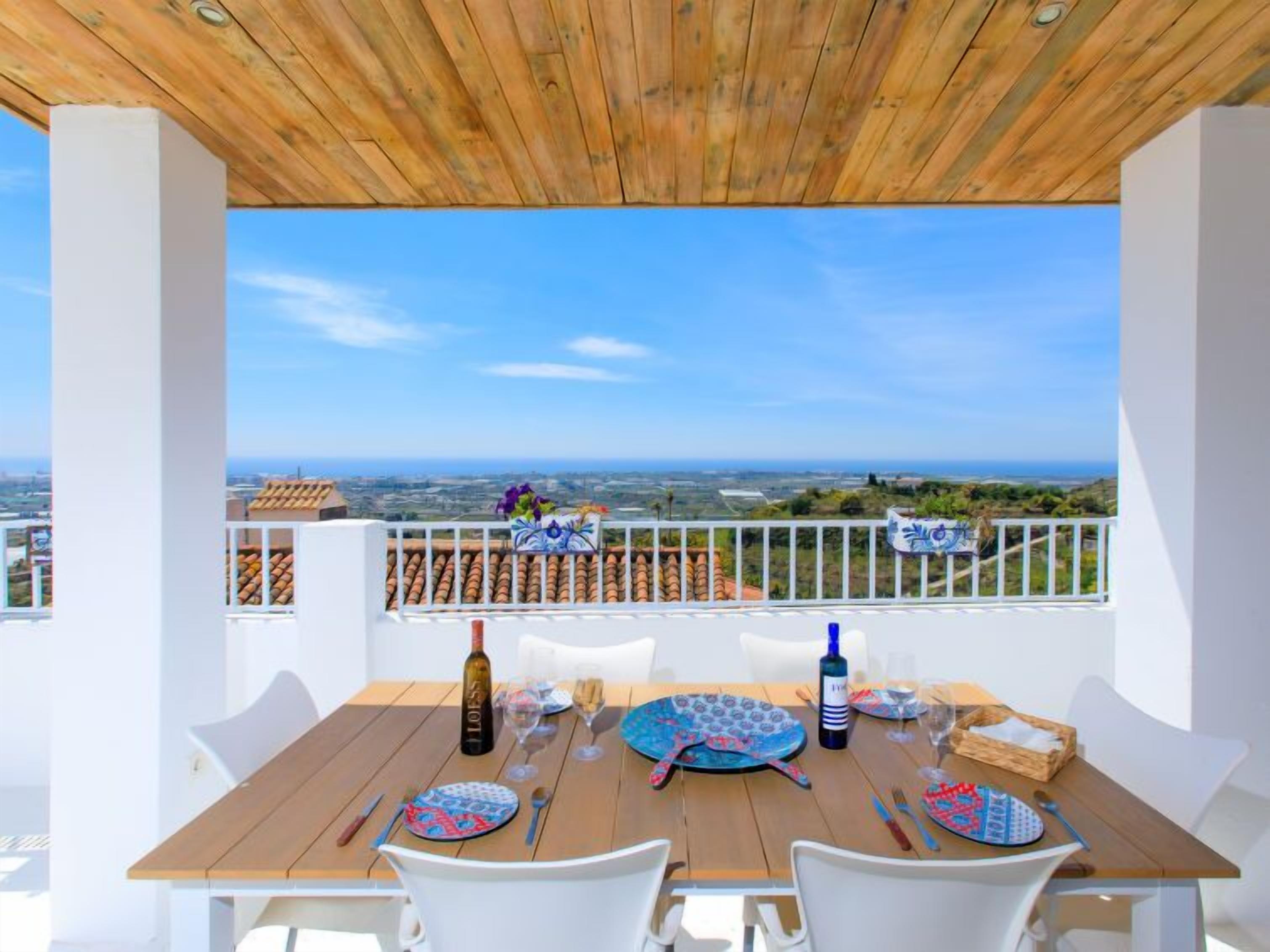 A wooden table set for two with a view of the sea and distant landscape.