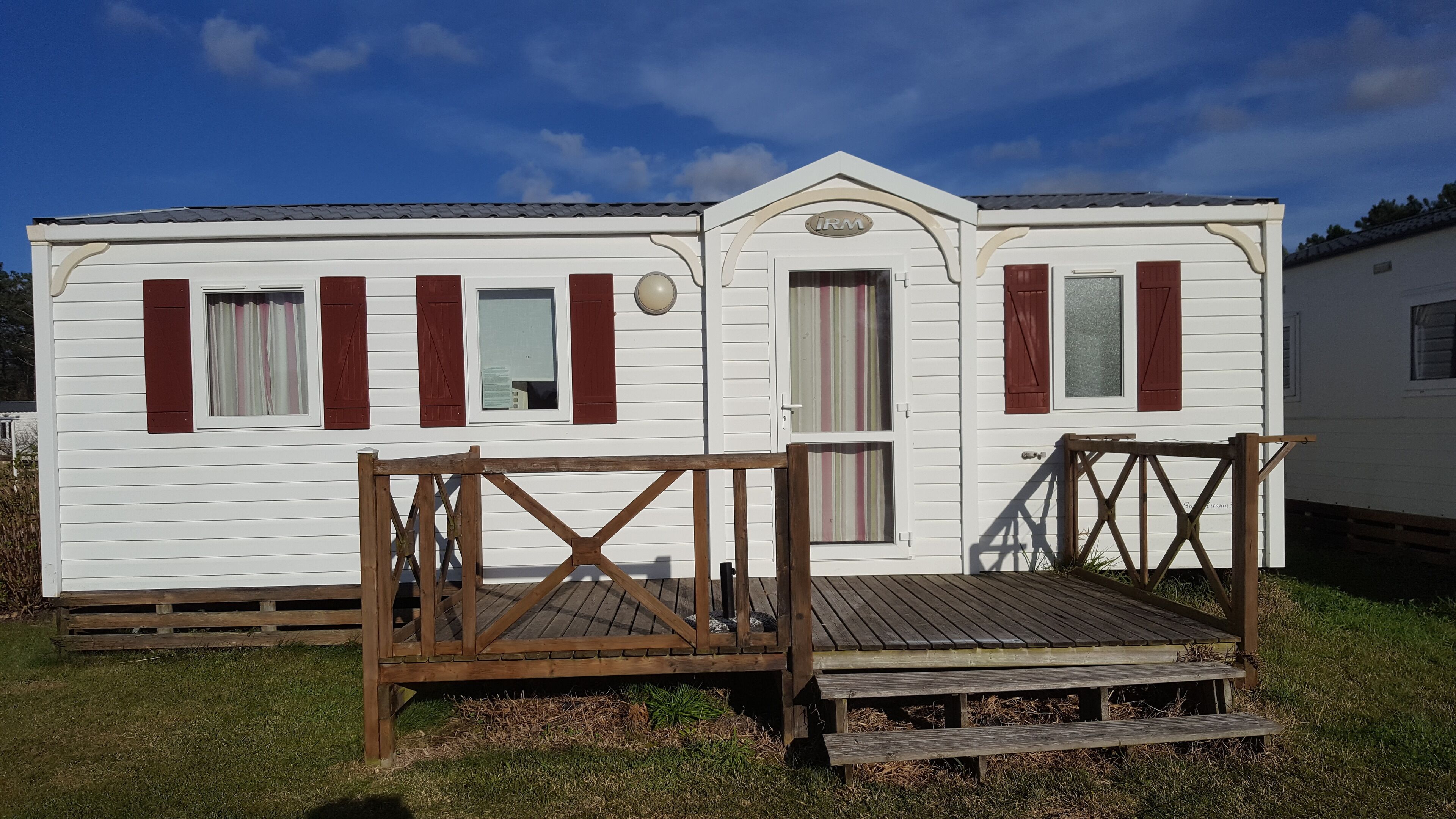A white mobile home with red shutters, a porch, and a small deck.