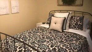 A neatly arranged bedroom with a black and white patterned bedspread, a metal bed frame, and a small bedside table with a lamp.