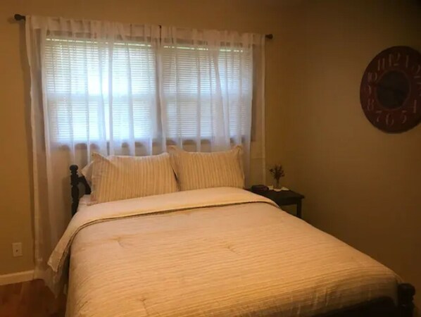 A bedroom with a bed, curtains, a clock, and a nightstand with a vase.
