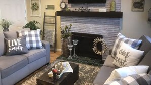 A living room with a grey sofa, a coffee table with a decorative item, a fireplace, and a television mounted on the wall.