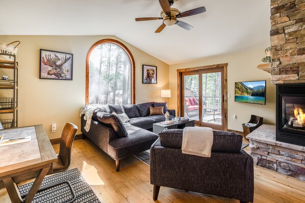 A cozy living room with a fireplace, a sofa, a dining table, and a large window. - Lake views, perfect proximity between town and the ski hill ! Immaculately furnished (Whitefish)