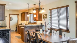 A spacious kitchen with wooden cabinets, a central island, and a dining area with a large table and chairs. - Lake views, perfect proximity between town and the ski hill ! Immaculately furnished (Whitefish)