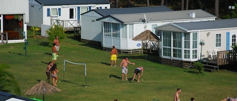 A recreational area with a netted volleyball court, a small pool, and several beach chairs and umbrellas.