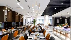 A modern dining area with long tables, orange and black chairs, and a buffet on the right. - Hotel Jialong By Jingling (Hefei)