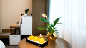 A modern hotel room with a wooden table, a white refrigerator, a small seating area, and a potted plant. - Hotel Jialong By Jingling (Hefei)