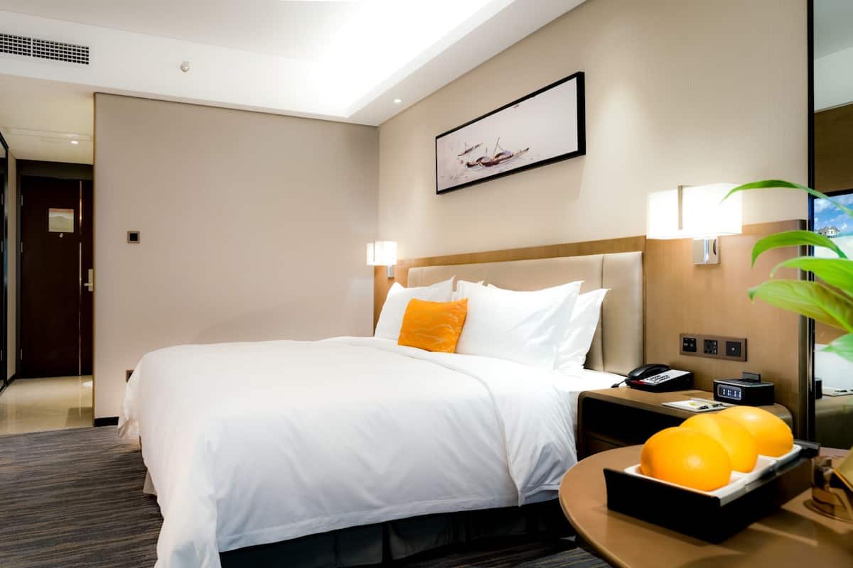 Ein Hotelzimmer mit einem großen Bett, einem Schreibtisch mit Telefon und Lampe sowie einem an der Wand befestigten Fernseher.