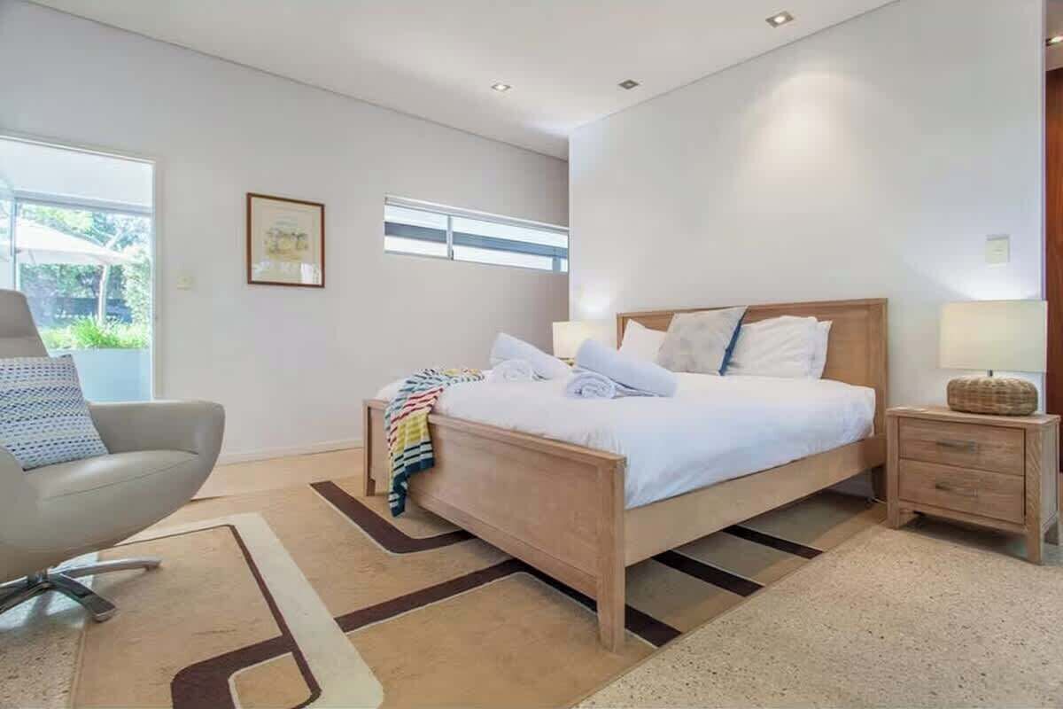 Une chambre à coucher moderne avec un lit, une table de chevet, une chaise et une fenêtre.