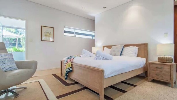 A modern bedroom with a bed, bedside table, chair, and a window. - Breezy Bay Retreat: Family Haven near Town & Beach (Dunsborough)