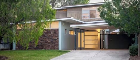 Una casa moderna de dos pisos con garaje cubierto, un muro de piedra y un césped bien cuidado.