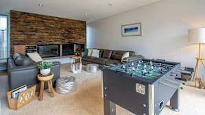 A modern living room with a foosball table, a sofa, a coffee table, and a fireplace. - Breezy Bay Retreat: Family Haven near Town & Beach (Dunsborough)