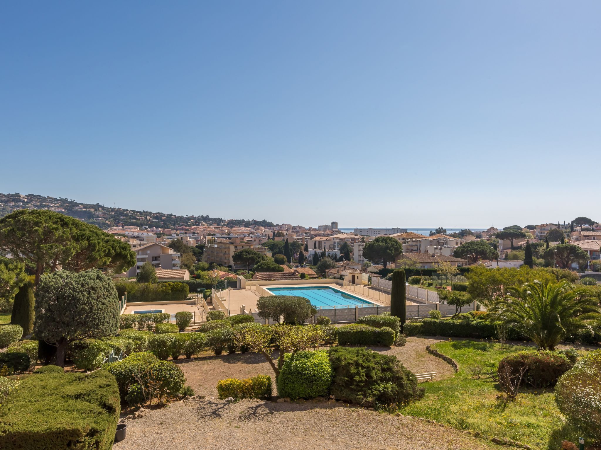 A residential area with a swimming pool surrounded by well-maintained gardens and a view of a coastal town.