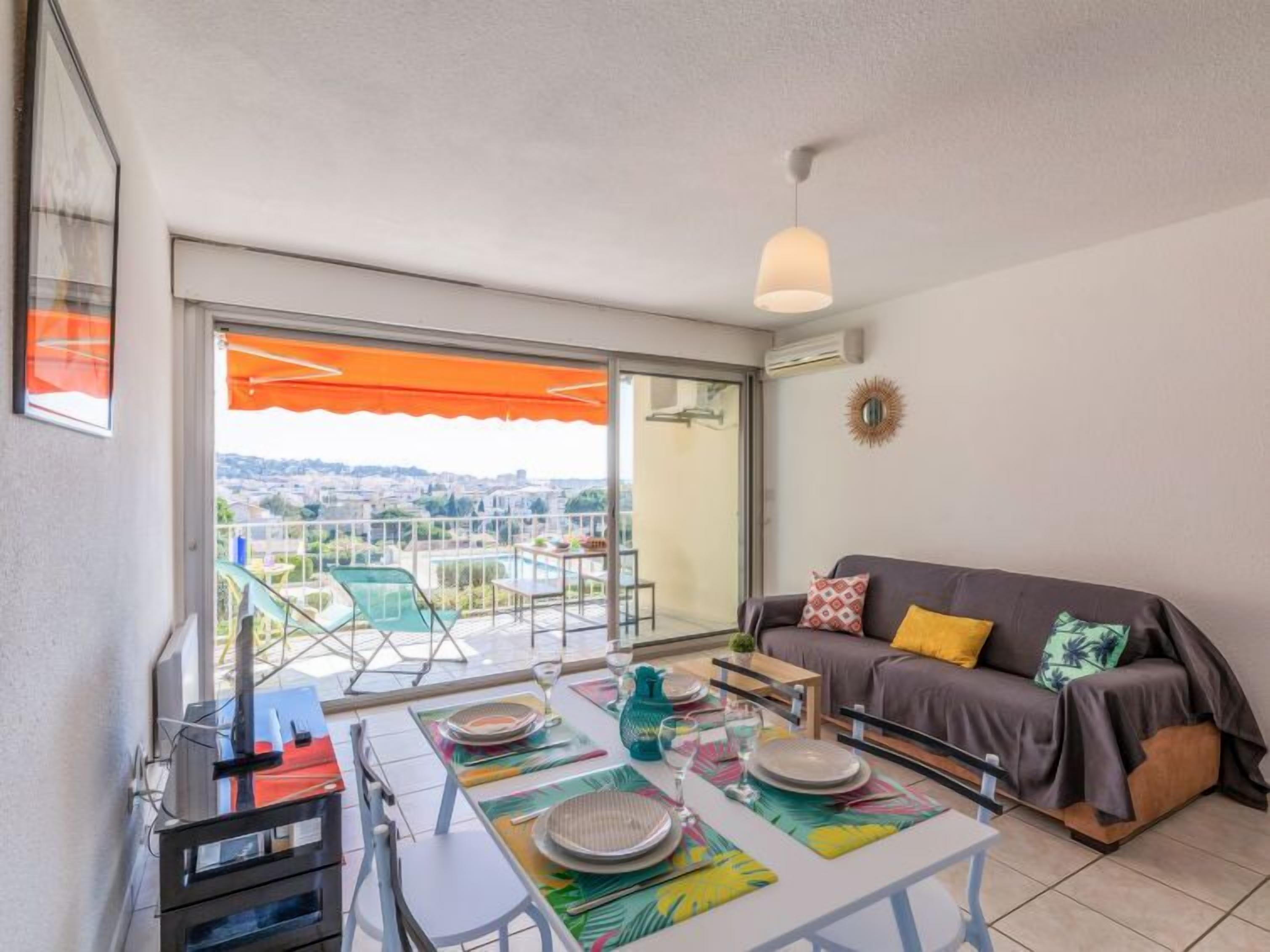 Un balcon avec une table dressée pour les repas, un canapé et une vue sur une piscine et le paysage urbain.