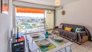 A balcony with a table set for dining, a sofa, and a view of a swimming pool and cityscape.
