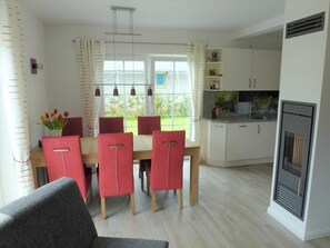 A modern kitchen with white cabinets, a built-in oven, and a dining area with a wooden table and red chairs.