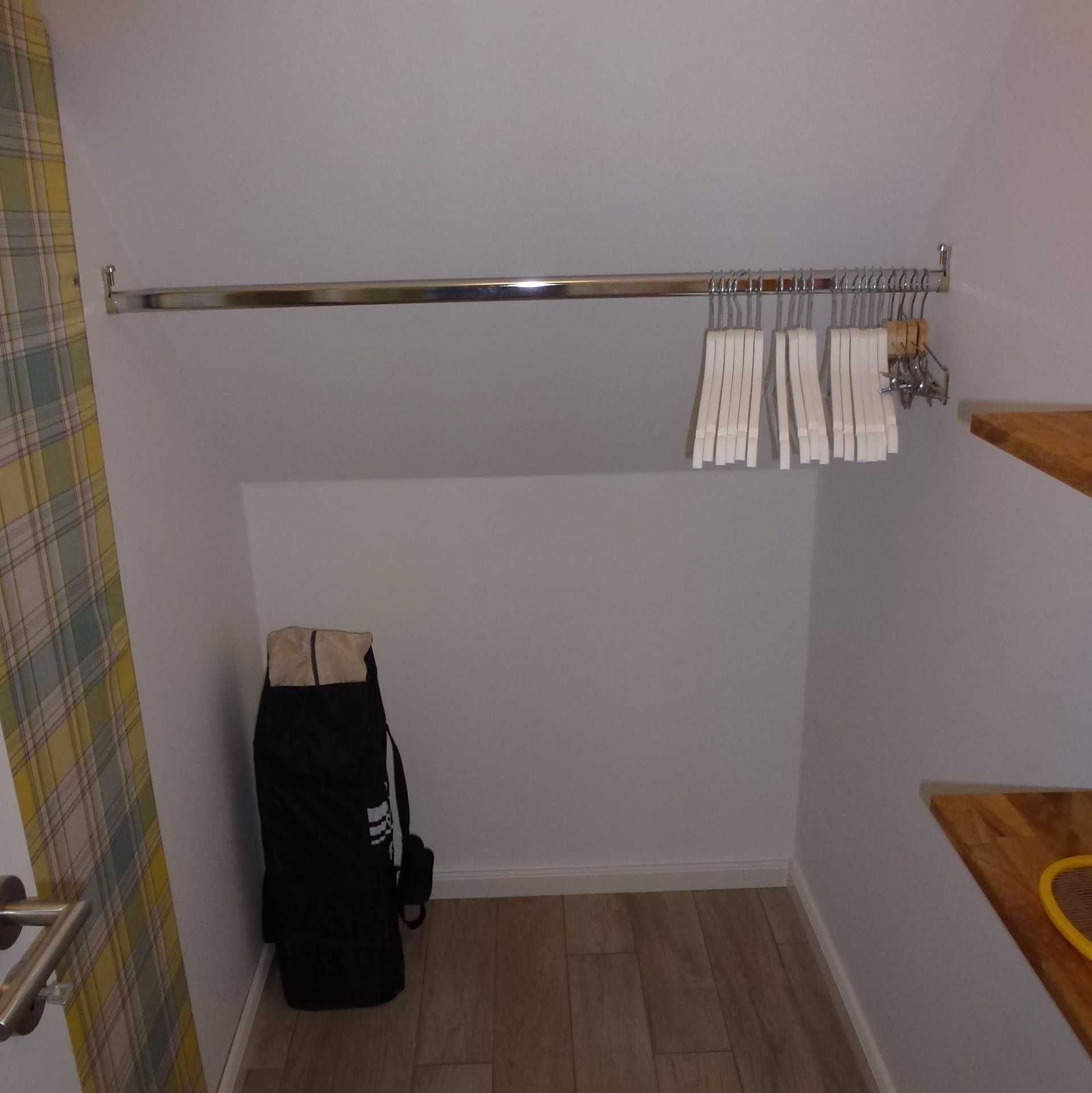 A small room with a wooden floor, a metal towel rack with white towels, and a black bag on the floor.