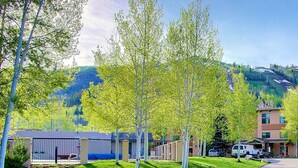 A hotel with a parking area, a building with a flat roof, and a mountain in the background. - Best Location-True Hike In/Out TH w/Slope Views-Heated Pool-HotTub-Gym-W/D in Unit-Fireplace-Updated (Steamboat Springs)