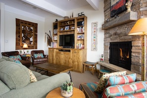 A cozy living room with a fireplace, a television, and a bookshelf filled with books and decorative items.