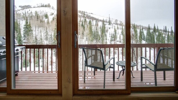 A wooden deck with two chairs and a table, overlooking a snowy mountain landscape. - Best Location-True Hike In/Out TH w/Slope Views-Heated Pool-HotTub-Gym-W/D in Unit-Fireplace-Updated (Steamboat Springs)
