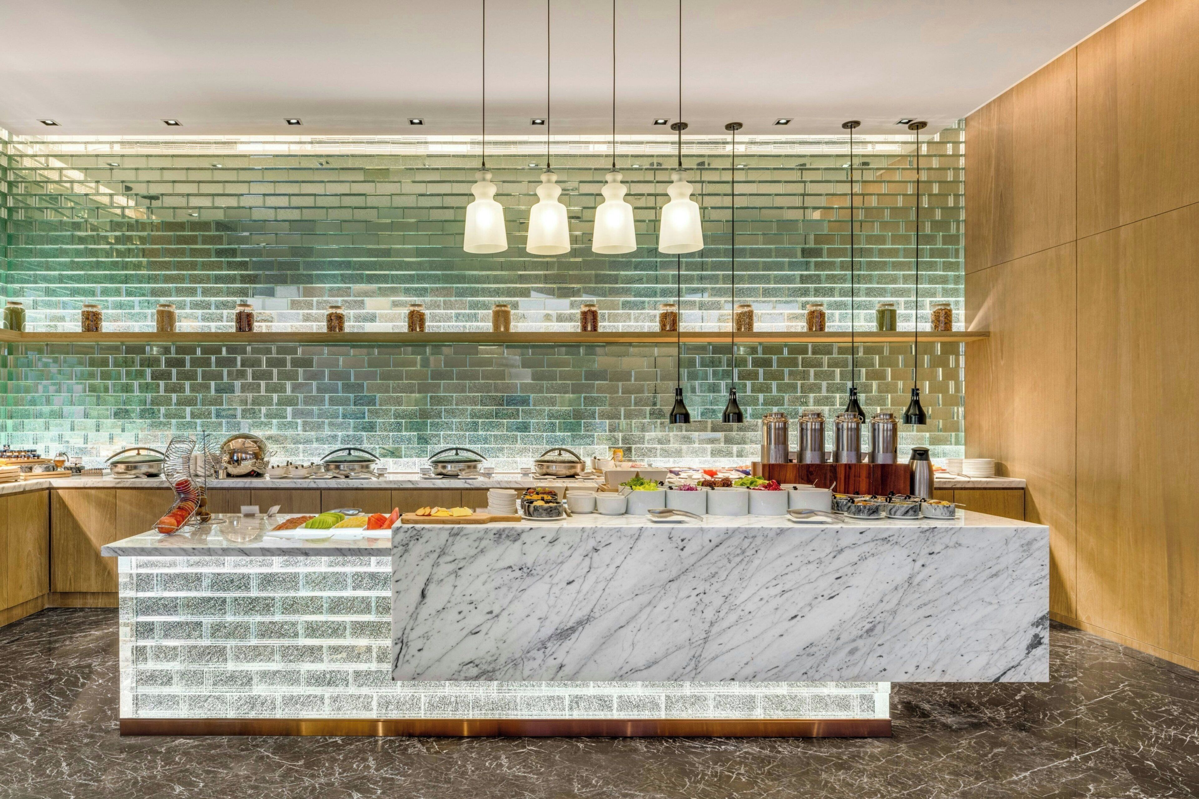 A modern kitchen with a marble island, glass backsplash, and hanging pendant lights.
