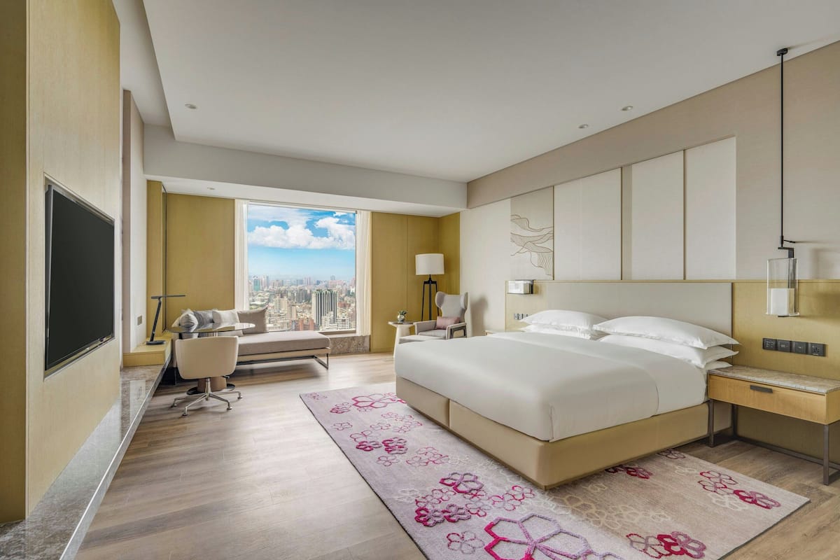 Una habitación de hotel moderna con una cama grande, un escritorio, una silla, un televisor y vistas a la ciudad.