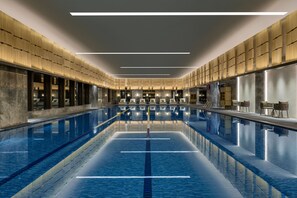Een groot binnenzwembad met duidelijke baanindeling, omgeven door houten lambrisering en moderne verlichting.