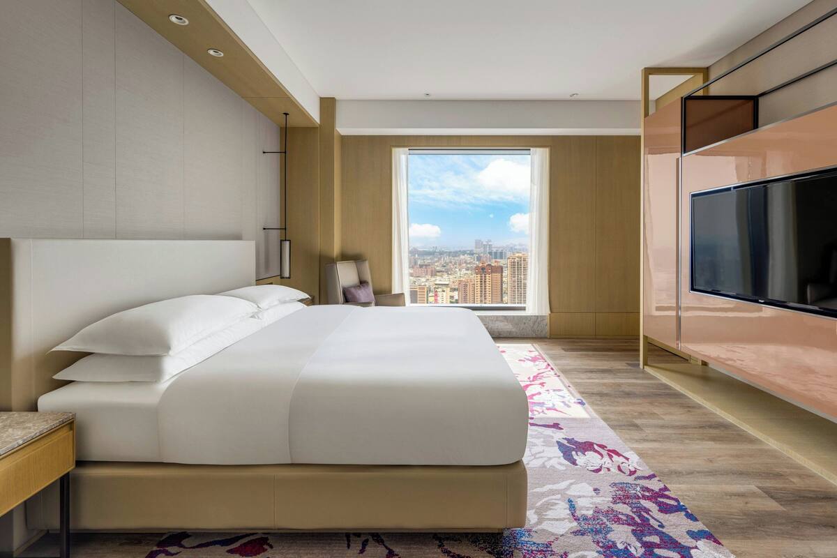 Una habitación de hotel con una cama grande, televisión, vistas a la ciudad y suelo de madera.
