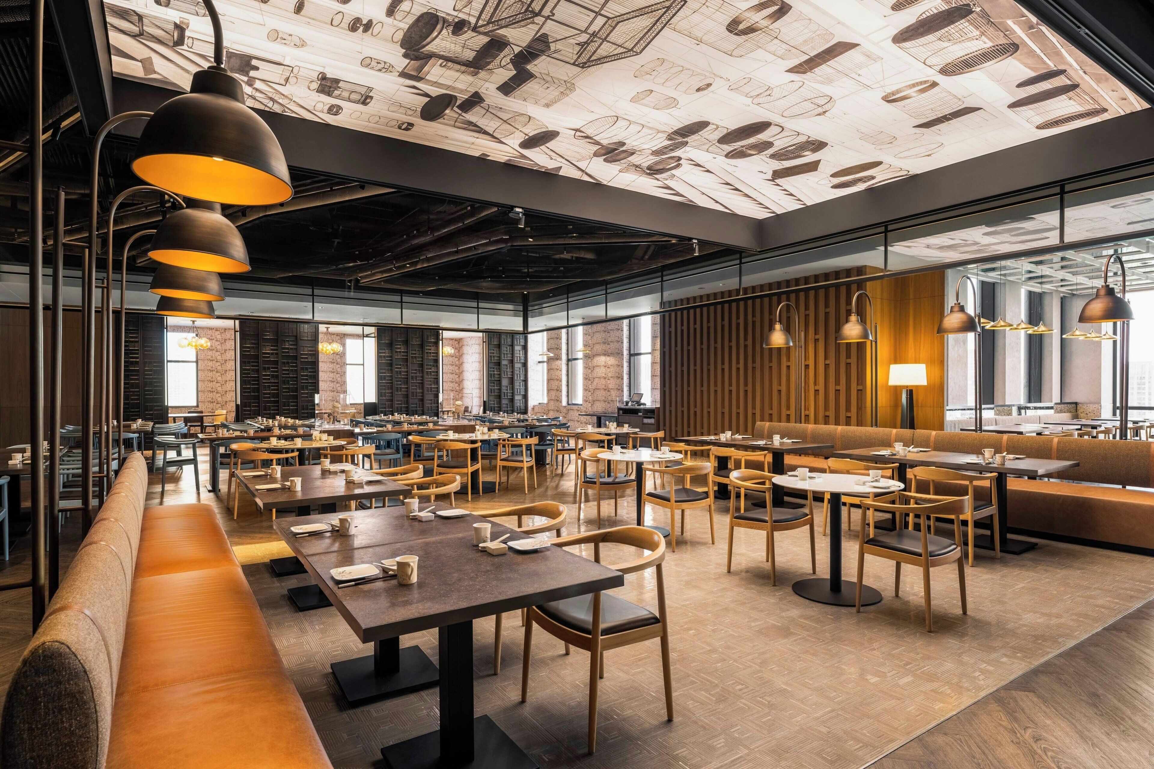 A spacious cafe with multiple seating areas, including tables and benches, and a ceiling with a unique design.