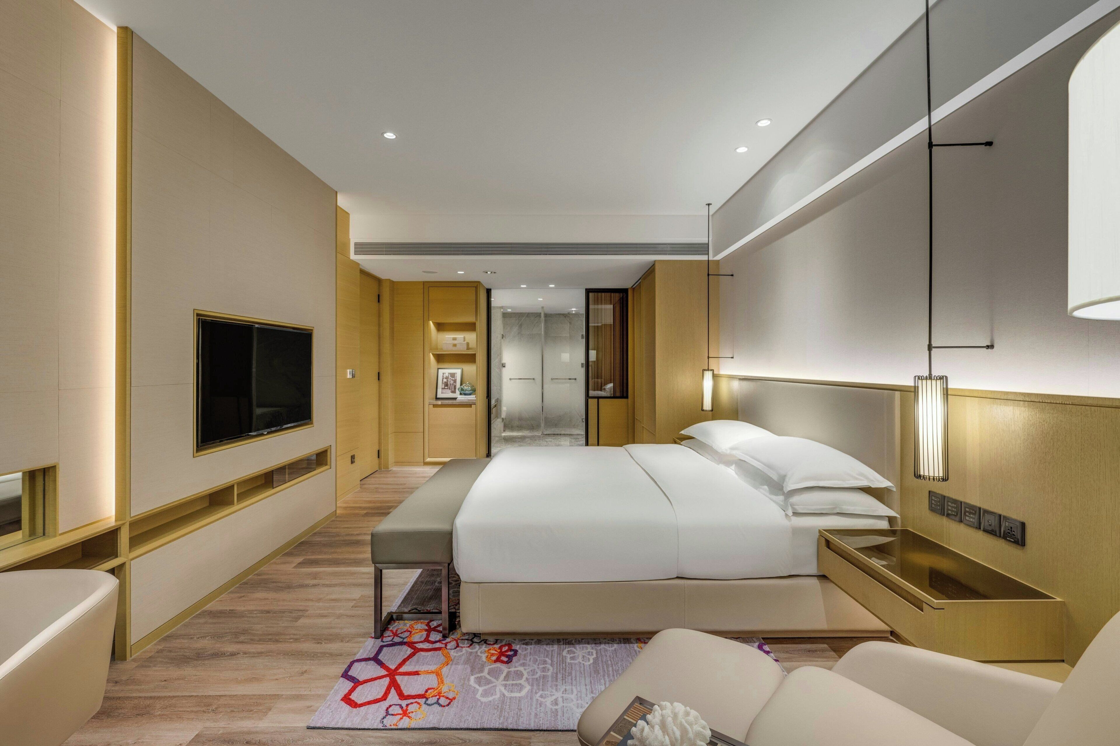 Una habitación de hotel moderna con una cama grande, mesitas de noche, un televisor de pantalla plana, un sofá y una alfombra decorativa.