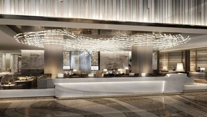 Un moderno vestíbulo de hotel con mostrador de recepción, zona de estar e instalación de iluminación única en el techo.