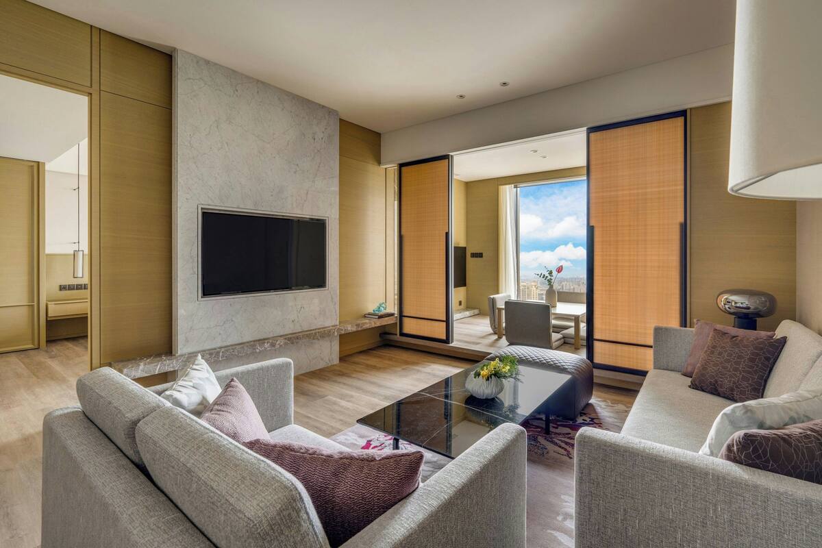 Una sala de estar moderna con un televisor de pantalla plana, dos sofás, una mesa de centro y un amplio ventanal corredera que da a un área exterior.