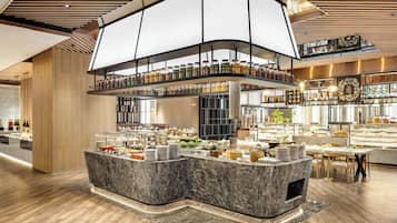 A modern hotel lobby with a marble reception desk, a glass display case with food items, and a high ceiling with wooden paneling.