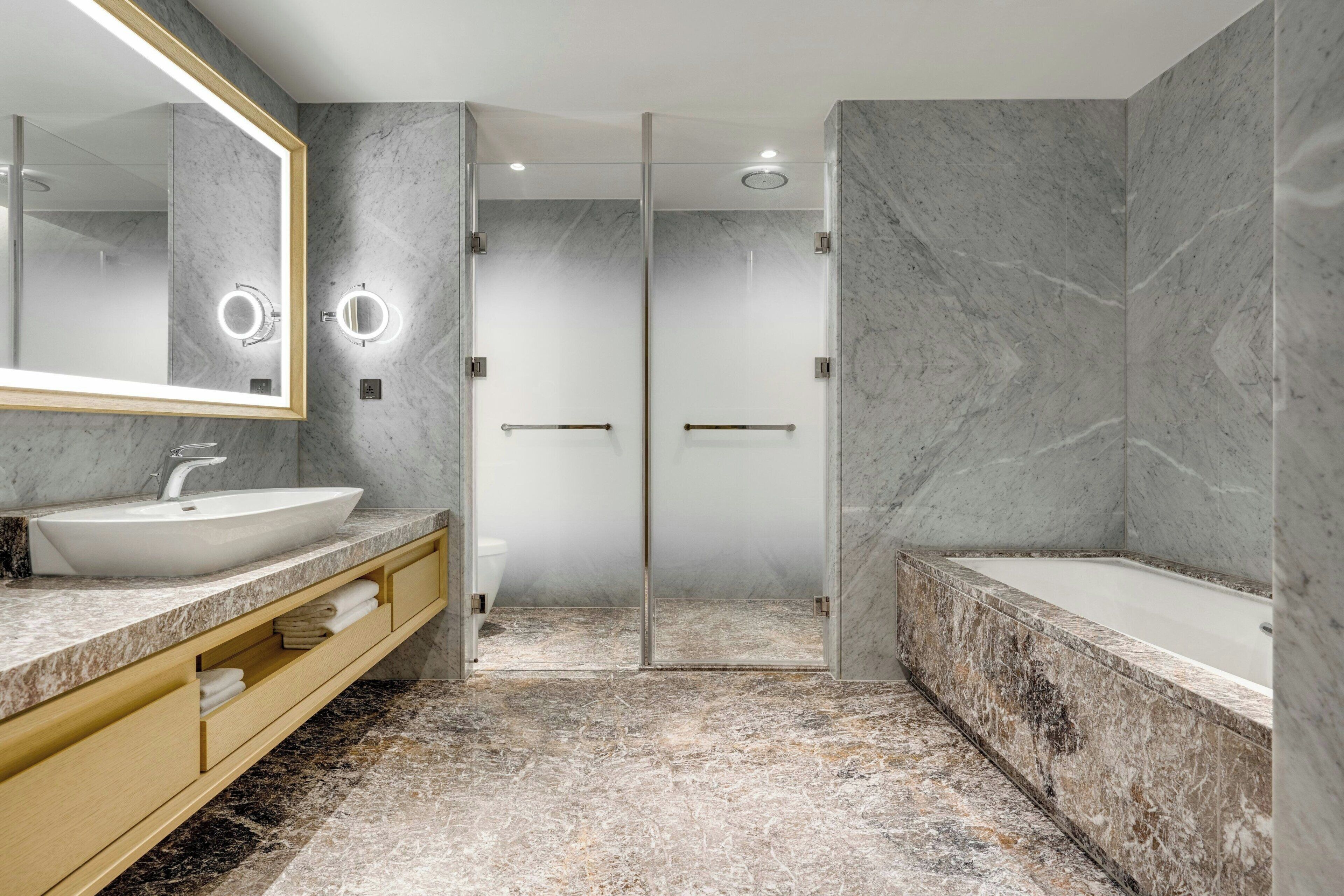 A modern bathroom with a large mirror, a sink, a bathtub, and a glass-enclosed shower.