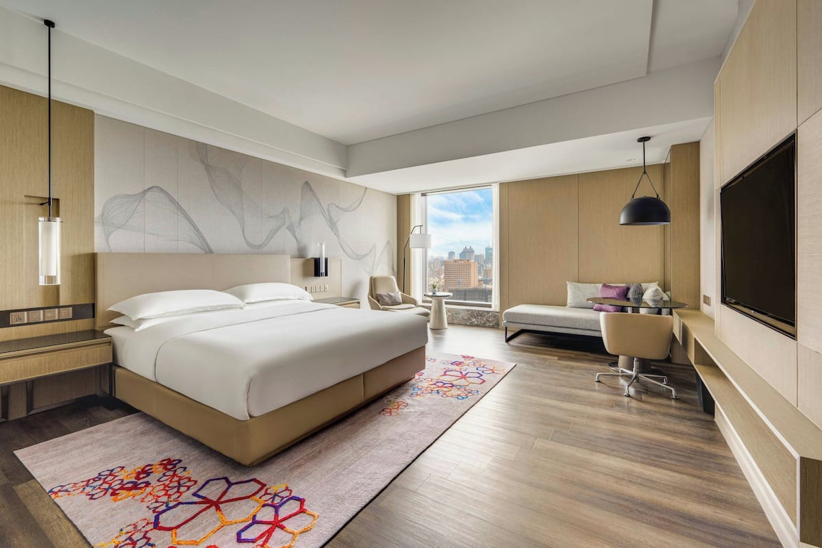 Una habitación de hotel moderna con una cama grande, televisión, zona de estar y vistas de la ciudad.