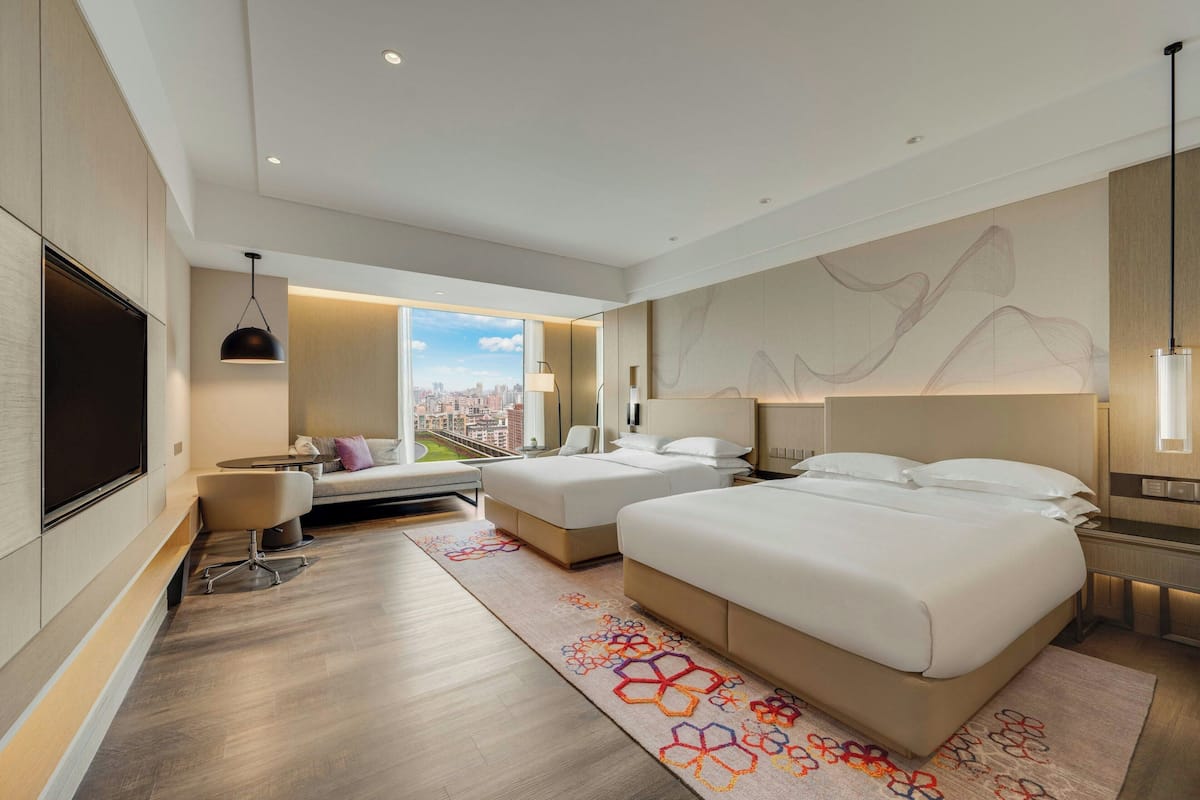 Una habitación de hotel moderna con dos camas, un sofá, un televisor y vista a la ciudad.