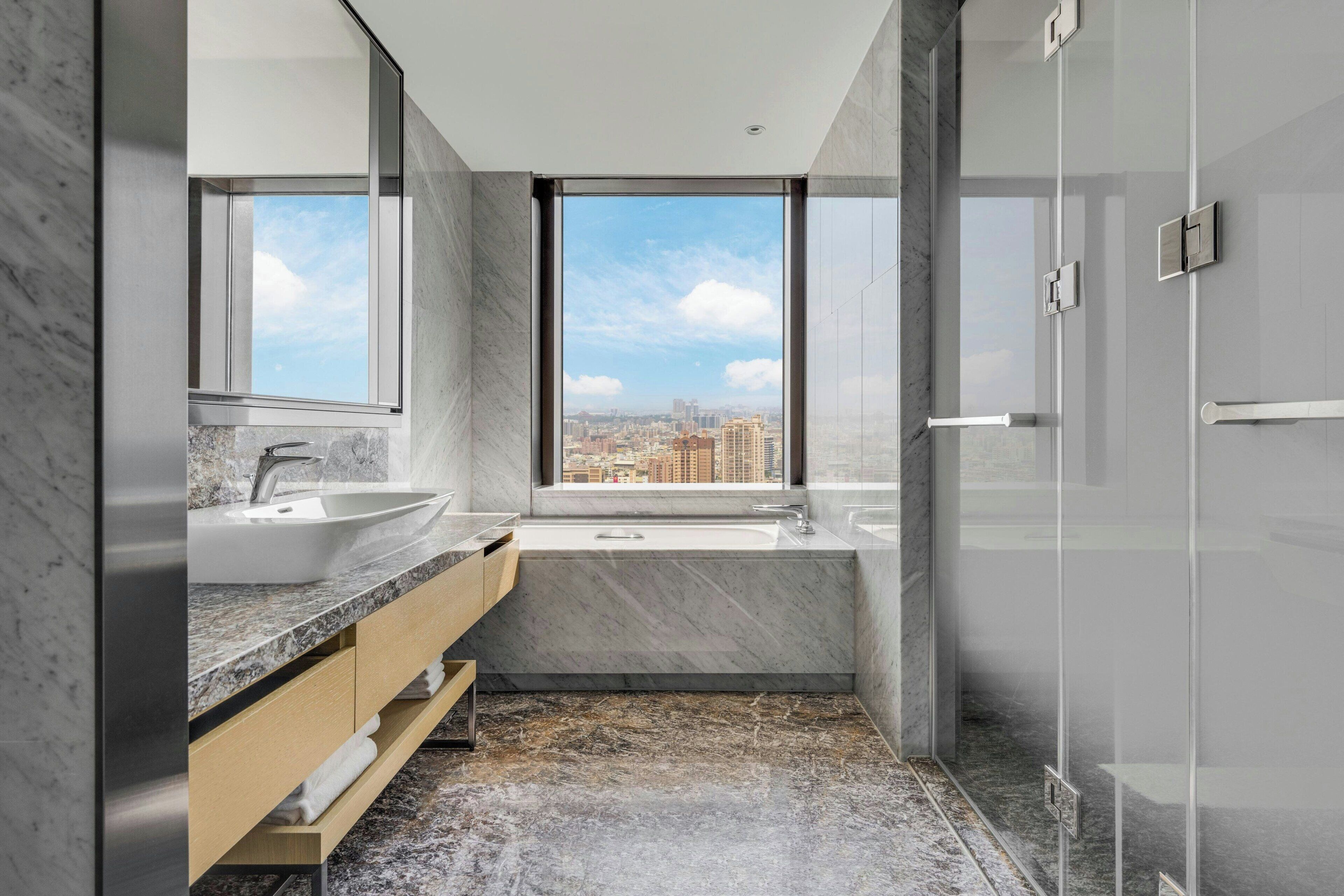 Un baño moderno con un ventanal grande, un lavabo, una bañera y un espejo.