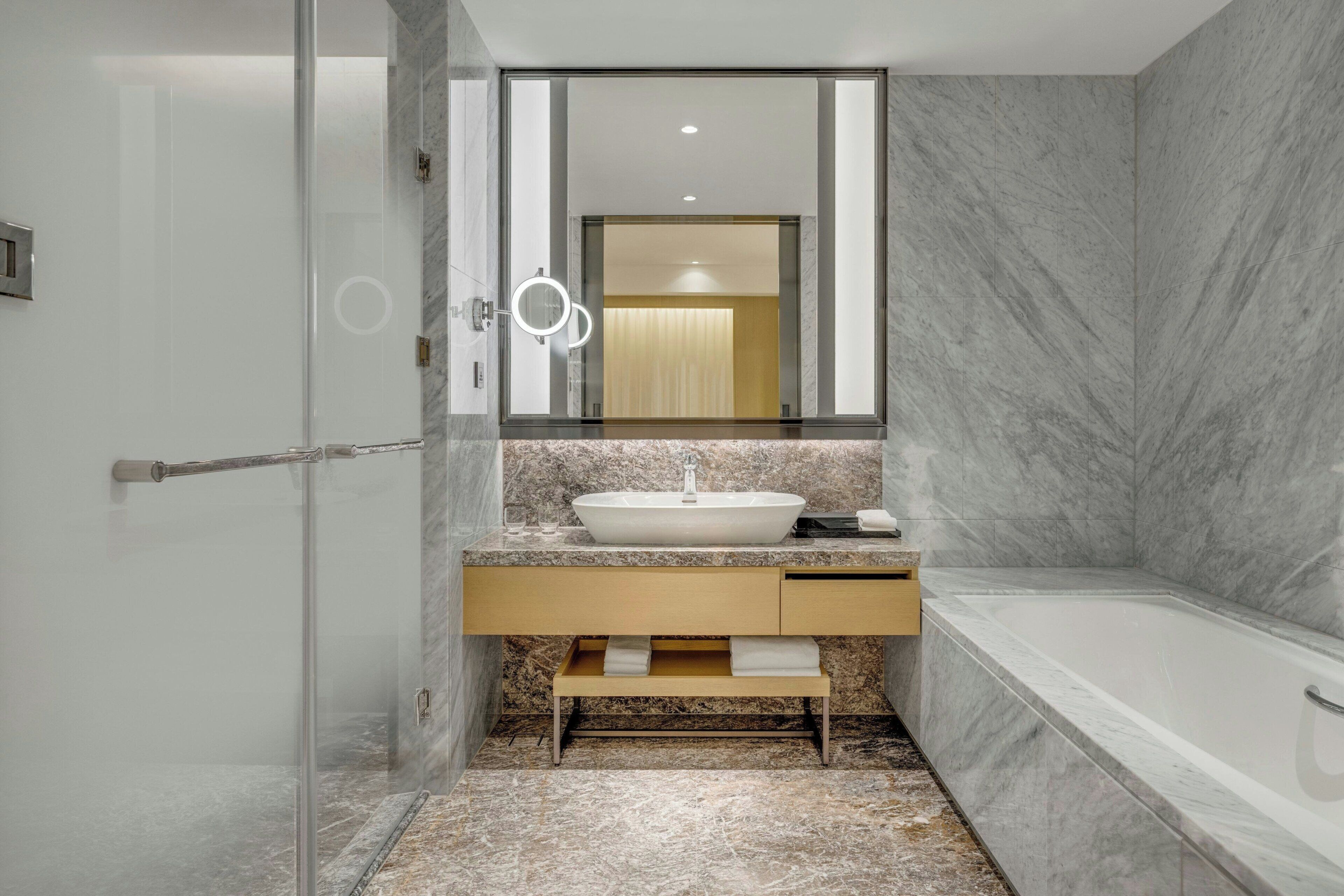 A modern bathroom with a glass shower enclosure, a marble sink, and a bathtub.