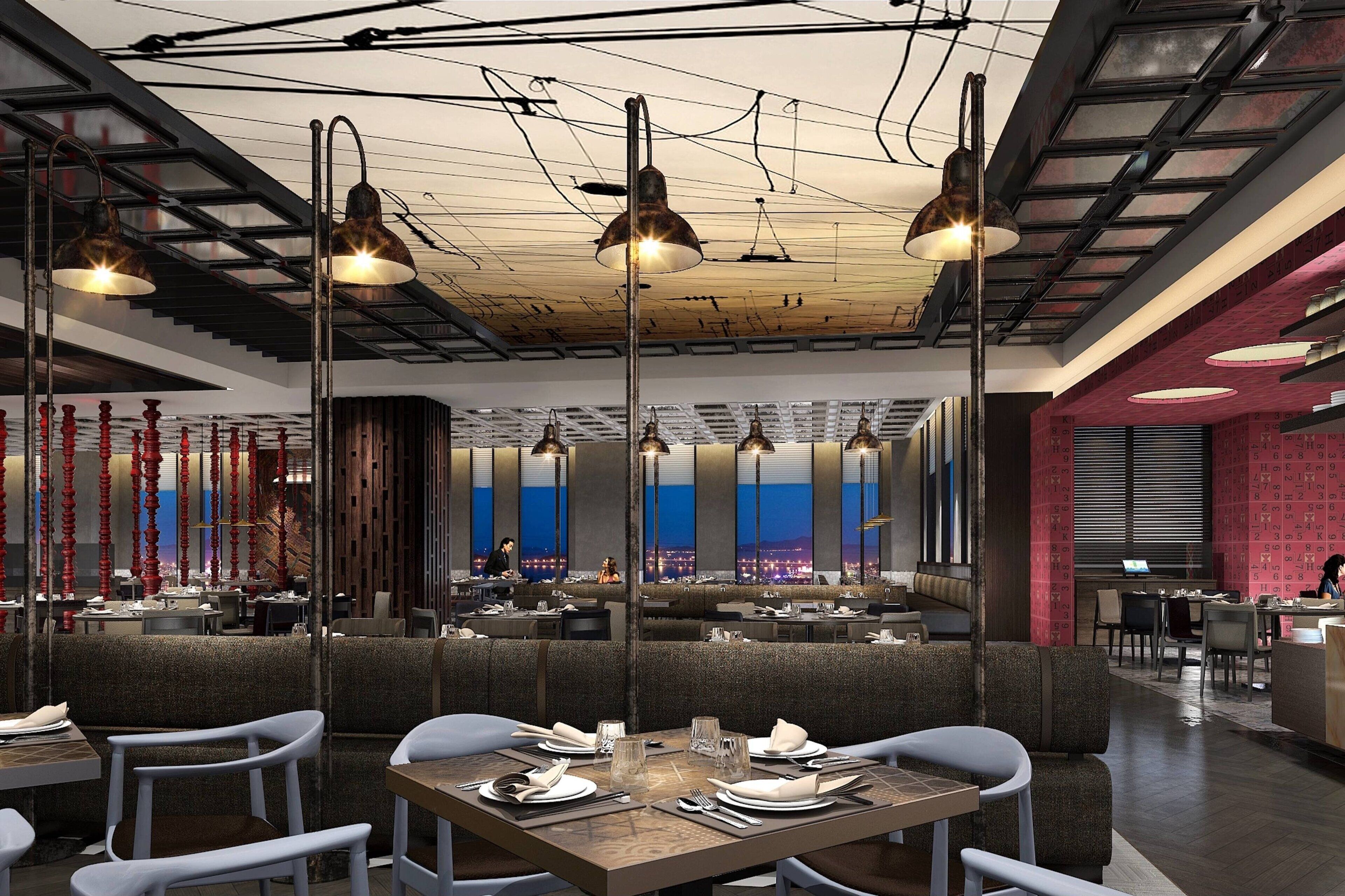 A modern restaurant with high ceilings, pendant lighting, and a view of the cityscape through large windows.
