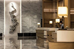 Een moderne lobby met een marmeren vloer, een unieke metalen sculptuur en een receptiebalie met lampen.