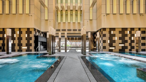 Zona de piscina con dos piscinas, un paseo central y vistas al interior del edificio.