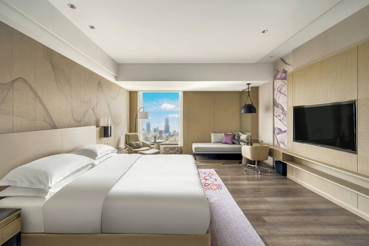Una habitación de hotel moderna con una cama grande, televisión, escritorio y vistas a la ciudad.