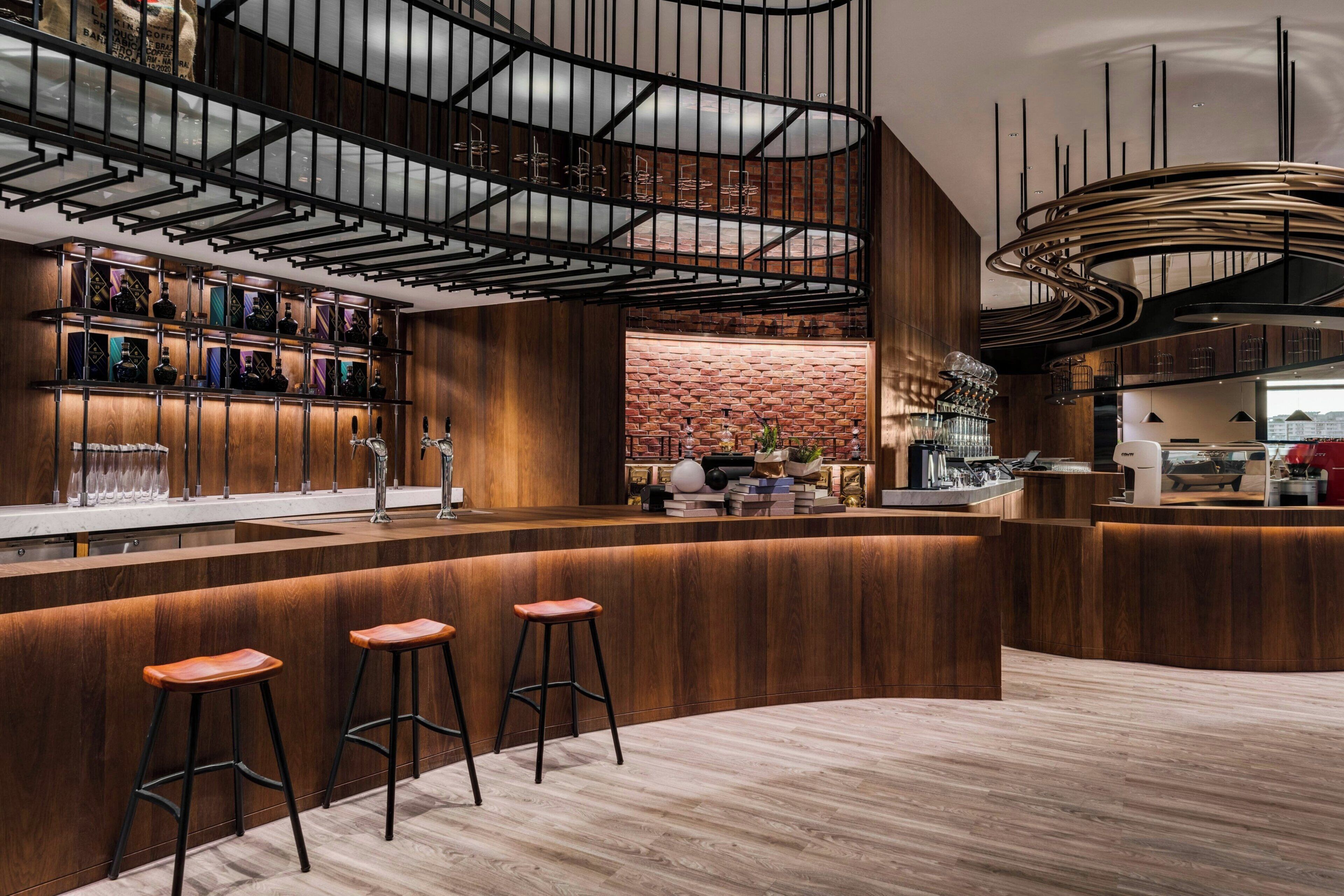 Una zona de bar moderna con detalles de madera, pared de ladrillo y un diseño de techo curvo.