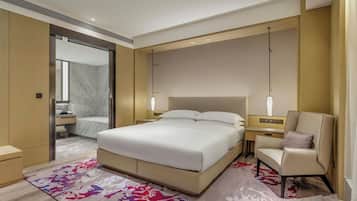A modern hotel room with a large bed, bedside tables, a chair, and a bathroom visible through an open door.