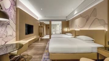 A hotel room with a bed, bedside tables, a TV, and a seating area with a glass table.