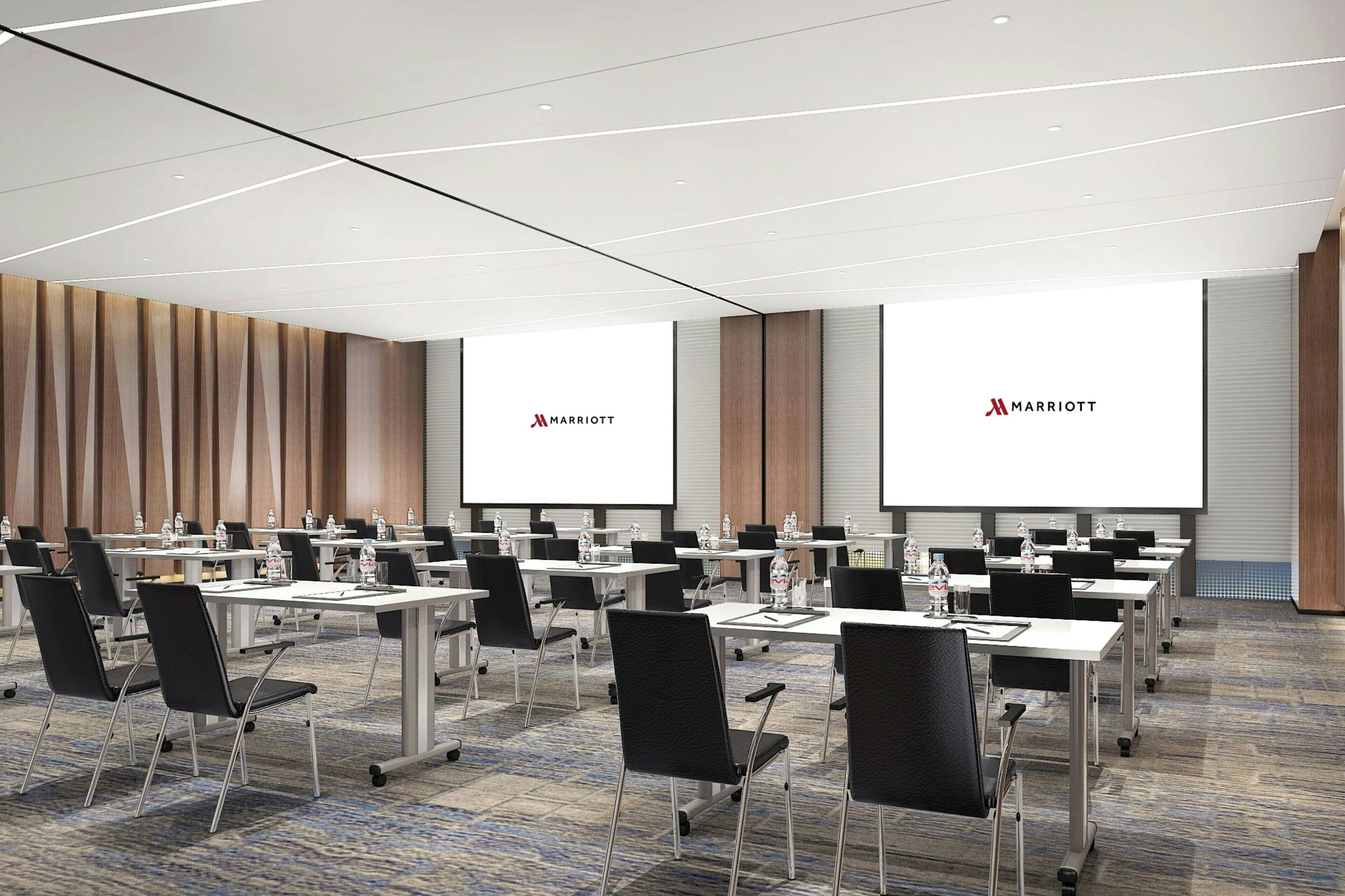 A conference room with multiple tables and chairs, a large screen, and the Marriott logo.