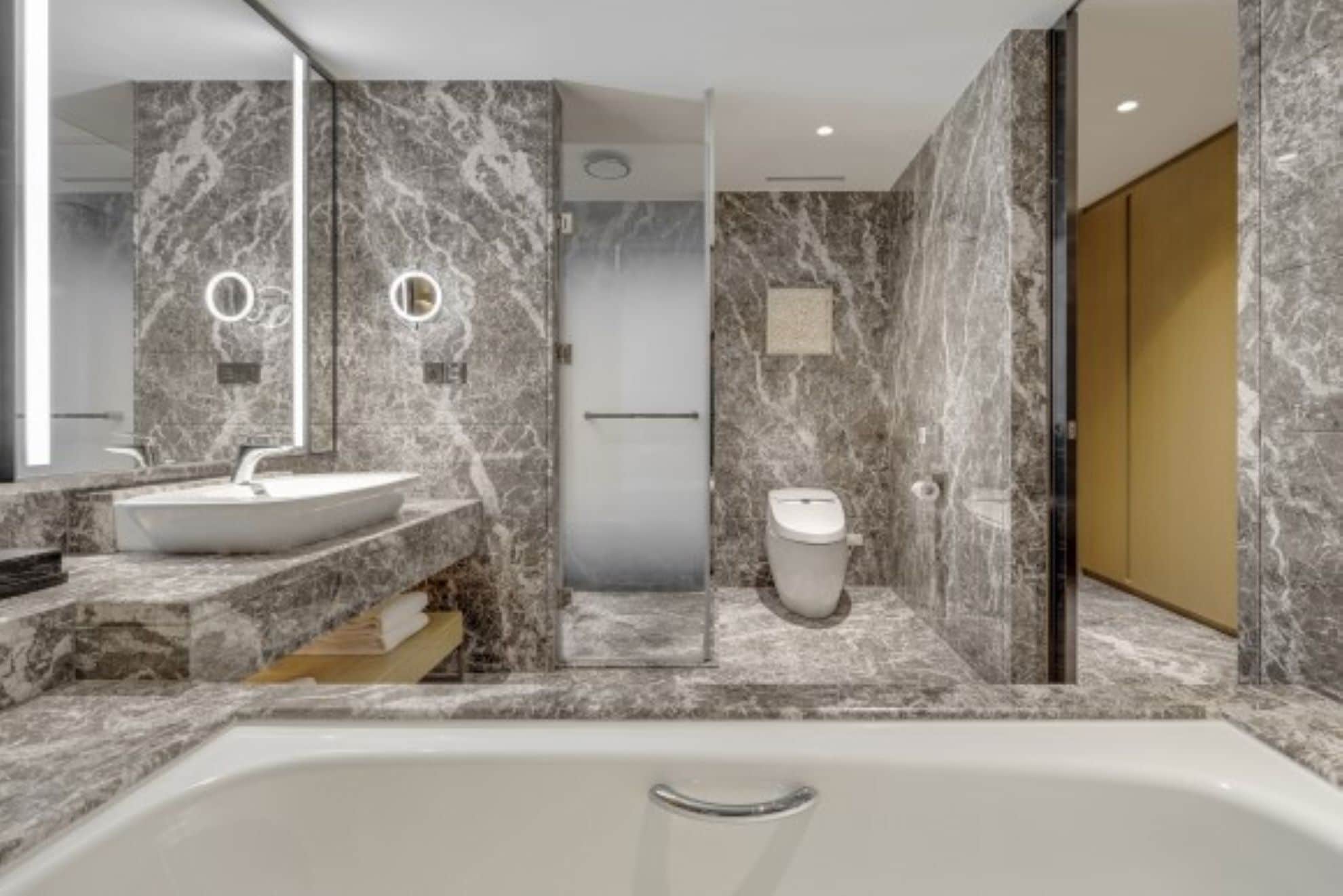 A modern bathroom with a marble sink, a bathtub, and a toilet.