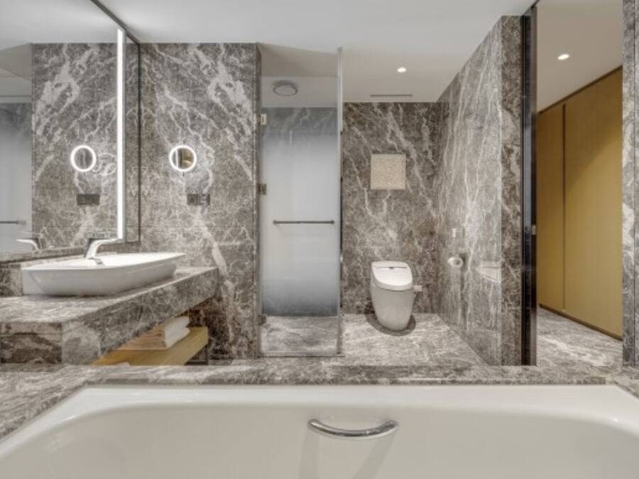 A modern bathroom with a marble sink, a bathtub, and a toilet.