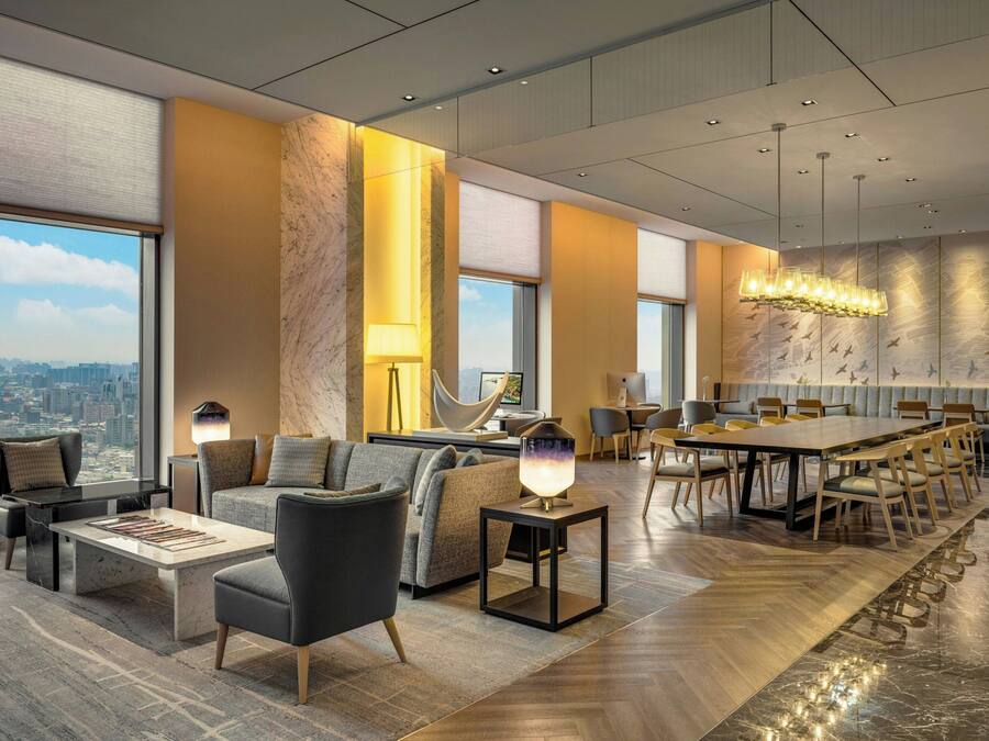 En modern hotellobby med ett stort matbord, bekväma sittplatser och utsikt över staden.