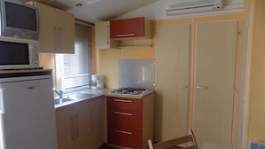 Cocina compacta con microondas, estufa y refrigerador. Cuenta con una ventana con persianas, un lavamanos y una silla.
