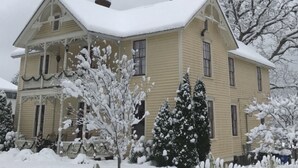 Una casa de dos pisos con techo cubierto de nieve y cerca de piquetes blancos.